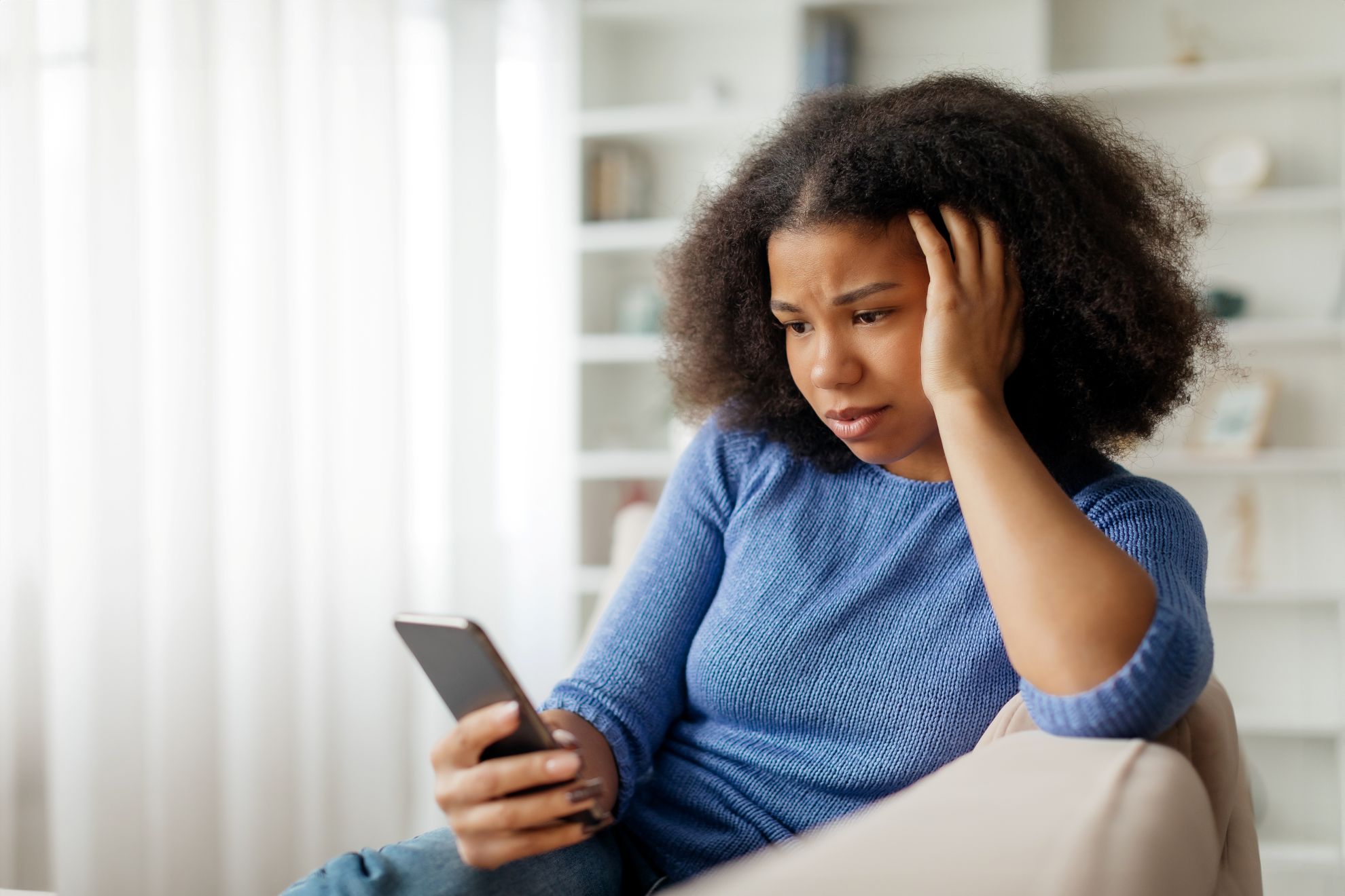AdobeStock_1093748662 Young woman sitting by a window, thinking
